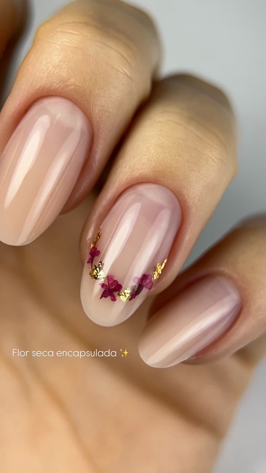 Nail art com flor seca encapsulada e detalhes em folha dourada